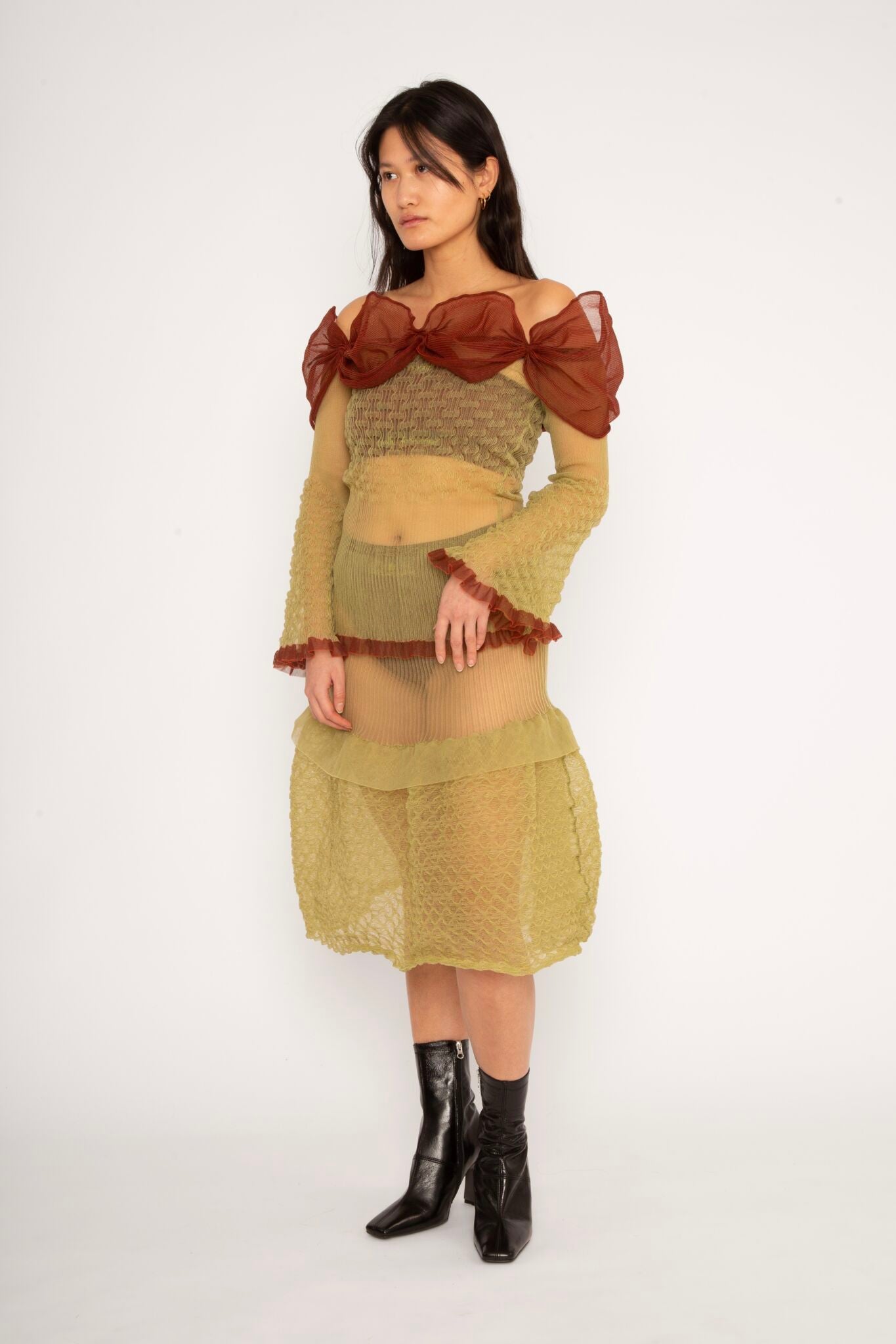 Bubble Bell Top in khaki and cherry red is a transparent knitted off-shoulder top in a ribbed bubble texture with ruffles and bell sleeves. The top has a close fit body with long sleeves and a voluminous adjustable neckline detailed with a melange rim with a logo in the back. The textile is lightweight, delicate and very flexible, meaning the dress adapts to body wearing it. The Bubble Bell Top is also available in teal and comes in 2 different sizes.