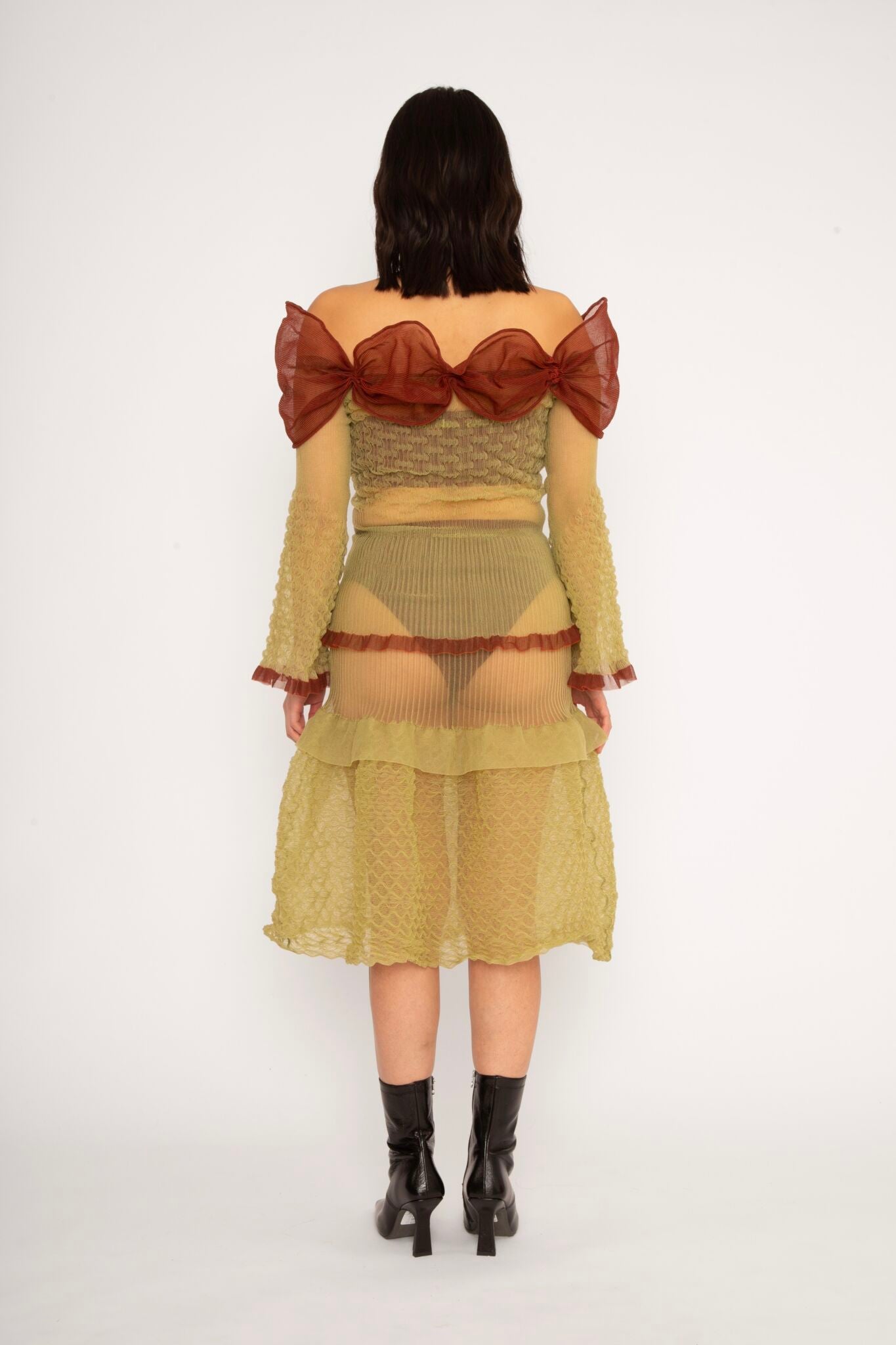 Bubble Bell Top in khaki and cherry red is a transparent knitted off-shoulder top in a ribbed bubble texture with ruffles and bell sleeves. The top has a close fit body with long sleeves and a voluminous adjustable neckline detailed with a melange rim with a logo in the back. The textile is lightweight, delicate and very flexible, meaning the dress adapts to body wearing it. The Bubble Bell Top is also available in teal and comes in 2 different sizes.