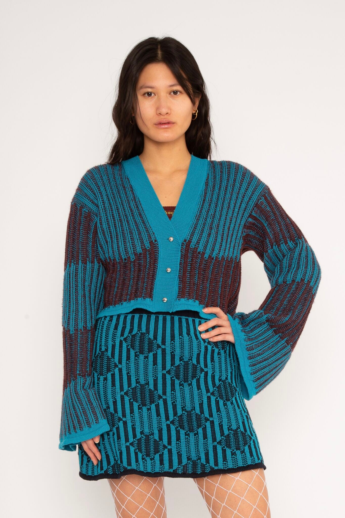 Wavy Wool Cardigan in turquoise and cherry red is a knitted cropped mohair cardigan with flared sleeves and all-over wavy stripes. Detailed with a heart in the back. The cardigan has a ribbed V-shaped neckline, a three-button closure and is cut for a slightly loose fit. The textile is fluffy, non-itchy and comfortable against the skin. The Wavy Wool Cardigan is also available in red and comes in 3 different sizes.