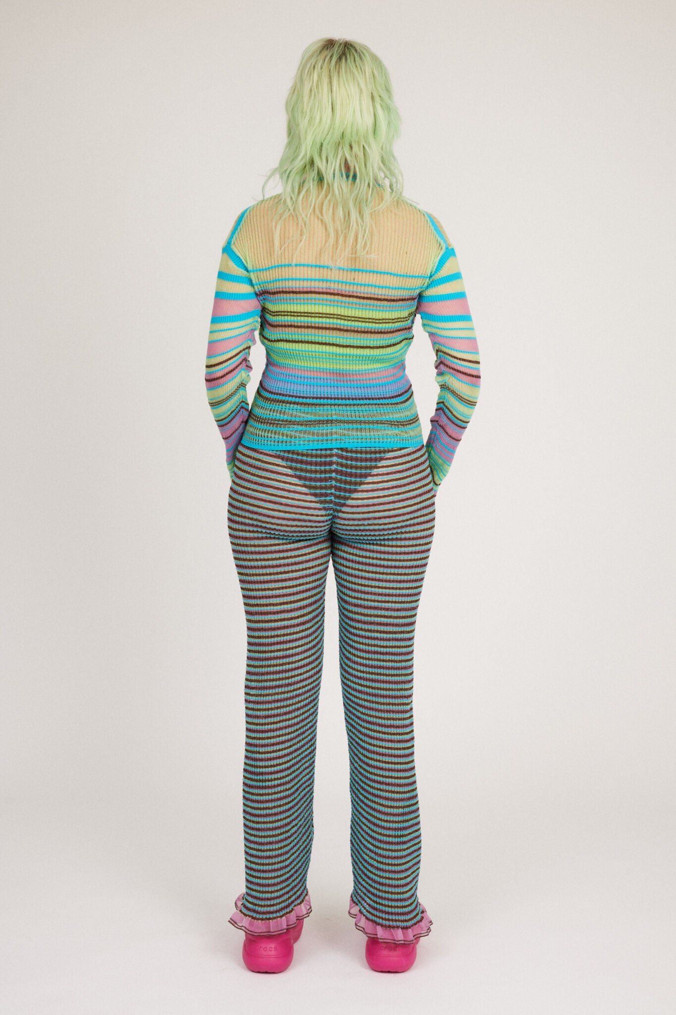 Sweet Secret Jumper in green and turquoise is a knitted transparent high neck jumper in all over bold stripes detailed with shimmery metallized yarn. The textile is lightweight, delicate and very flexible. The jumper has a body fitted silhouette that adapts to the body. Detailed with frills and a logo in the back of the neck.