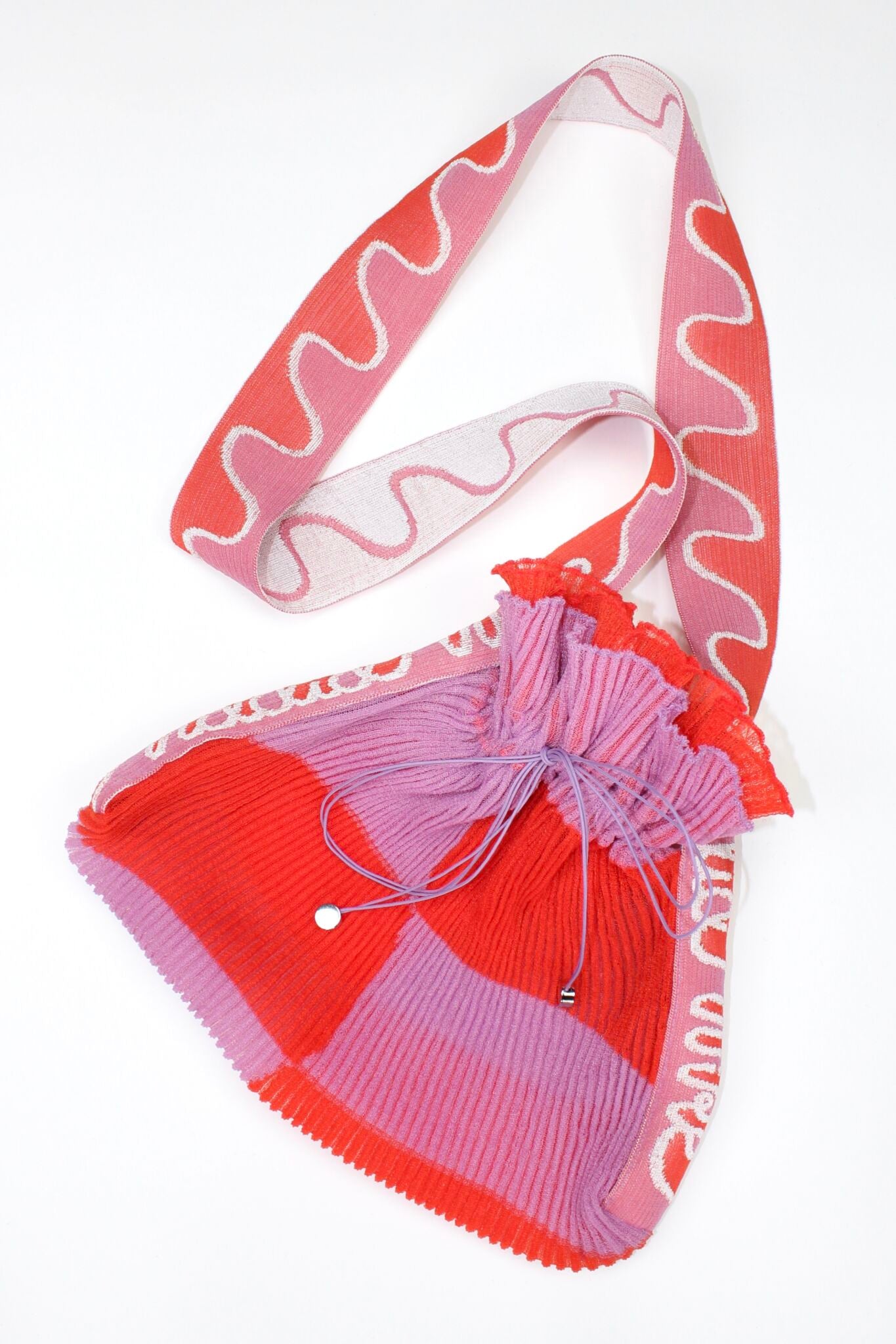 Twisted Frill Bag in coral red and lavender is a knitted transparent crossbody cinch bag in twisted chess stripes. Detailed with ruffles, a logo jacquard strap and an adjustable opening. The textile is lightweight, delicate and flexible and has ribbed texture.