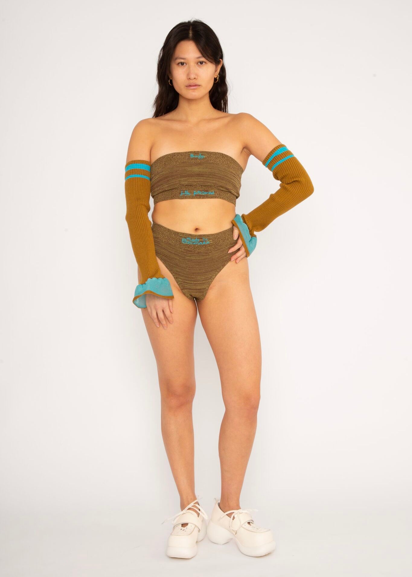 Wool Frills in hazel and turquoise are a knitted pair of frills in merino wool with a ribbed surface. Detailed with bold sporty stripes and a transparent ruffle. The textile is soft, non-itchy and very stretchy. Can be worn on both the arms as well as the legs. The Wool Frills are a functional styling piece, that will keep you warm. Available in 3 different colours.