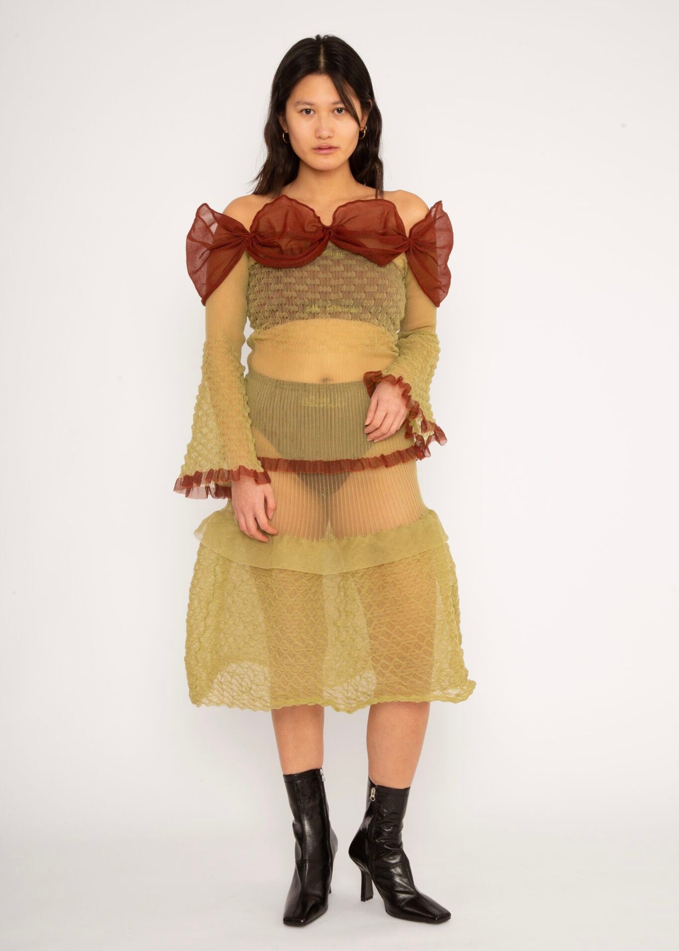 Bubble Bell Top in khaki and cherry red is a transparent knitted off-shoulder top in a ribbed bubble texture with ruffles and bell sleeves. The top has a close fit body with long sleeves and a voluminous adjustable neckline detailed with a melange rim with a logo in the back. The textile is lightweight, delicate and very flexible, meaning the dress adapts to body wearing it. The Bubble Bell Top is also available in teal and comes in 2 different sizes.