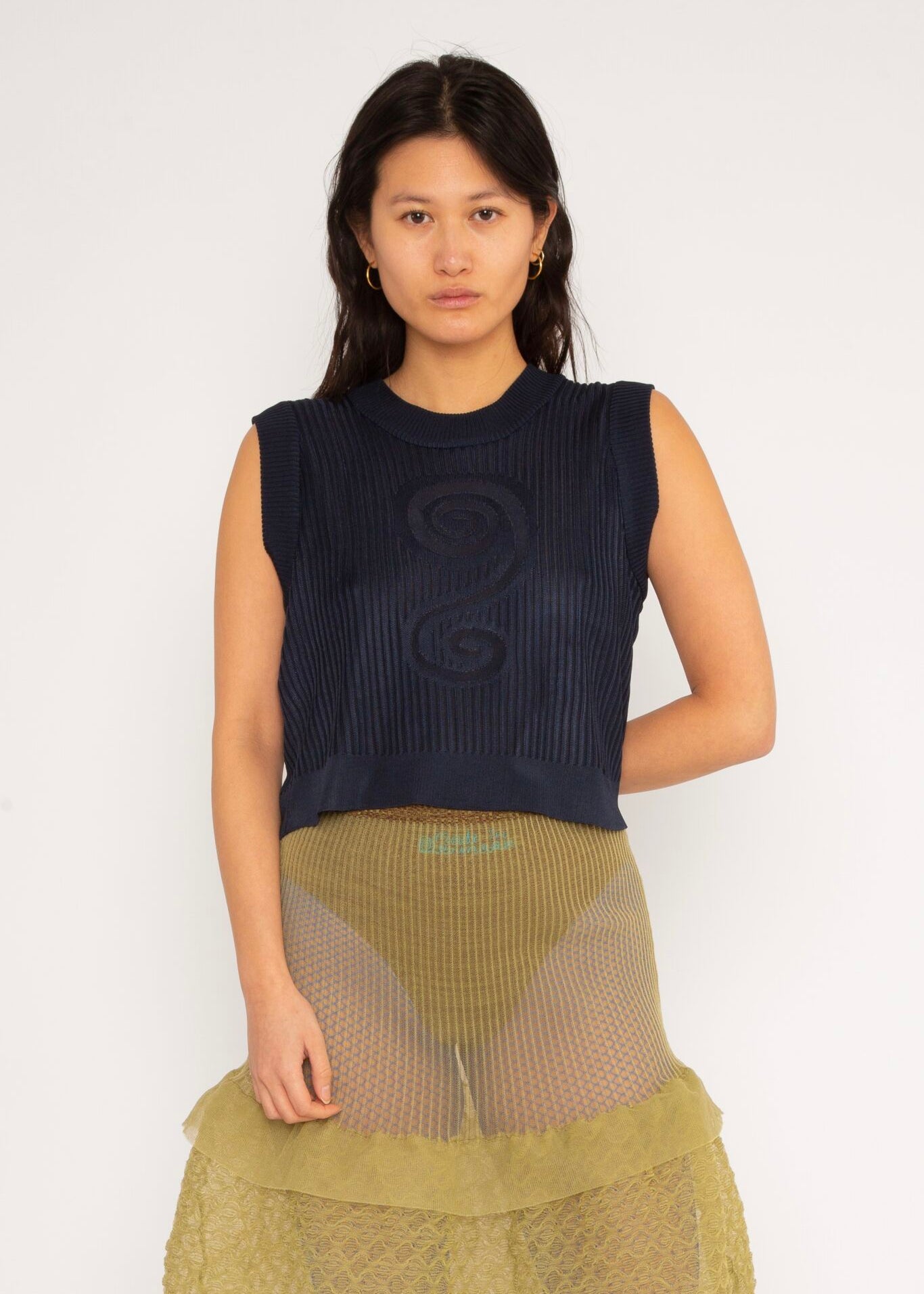 Spiral Top in navy is a knitted cropped crew neck top with spiral artwork. The textile has a shine to it and is lightweight with a smooth and soft feel against the body. The top has a slightly loose fit and is detailed with ribbed rims. The Spiral Top is available in 3 different sizes.
