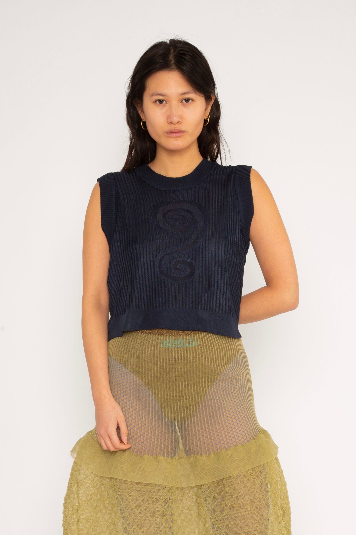 Spiral Top in navy is a knitted cropped crew neck top with spiral artwork. The textile has a shine to it and is lightweight with a smooth and soft feel against the body. The top has a slightly loose fit and is detailed with ribbed rims. The Spiral Top is available in 3 different sizes.