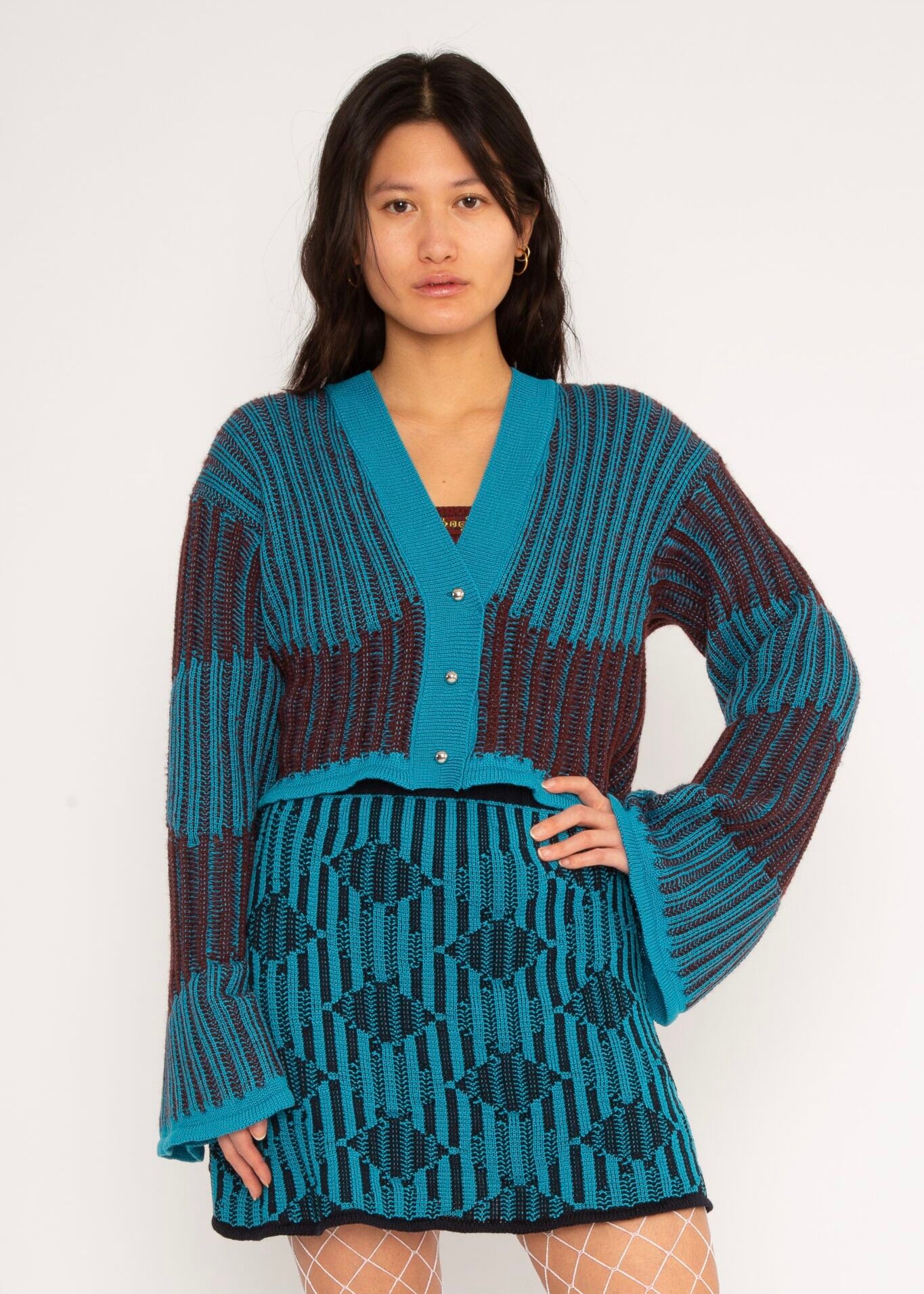 Wavy Wool Cardigan in turquoise and cherry red is a knitted cropped mohair cardigan with flared sleeves and all-over wavy stripes. Detailed with a heart in the back. The cardigan has a ribbed V-shaped neckline, a three-button closure and is cut for a slightly loose fit. The textile is fluffy, non-itchy and comfortable against the skin. The Wavy Wool Cardigan is also available in red and comes in 3 different sizes.
