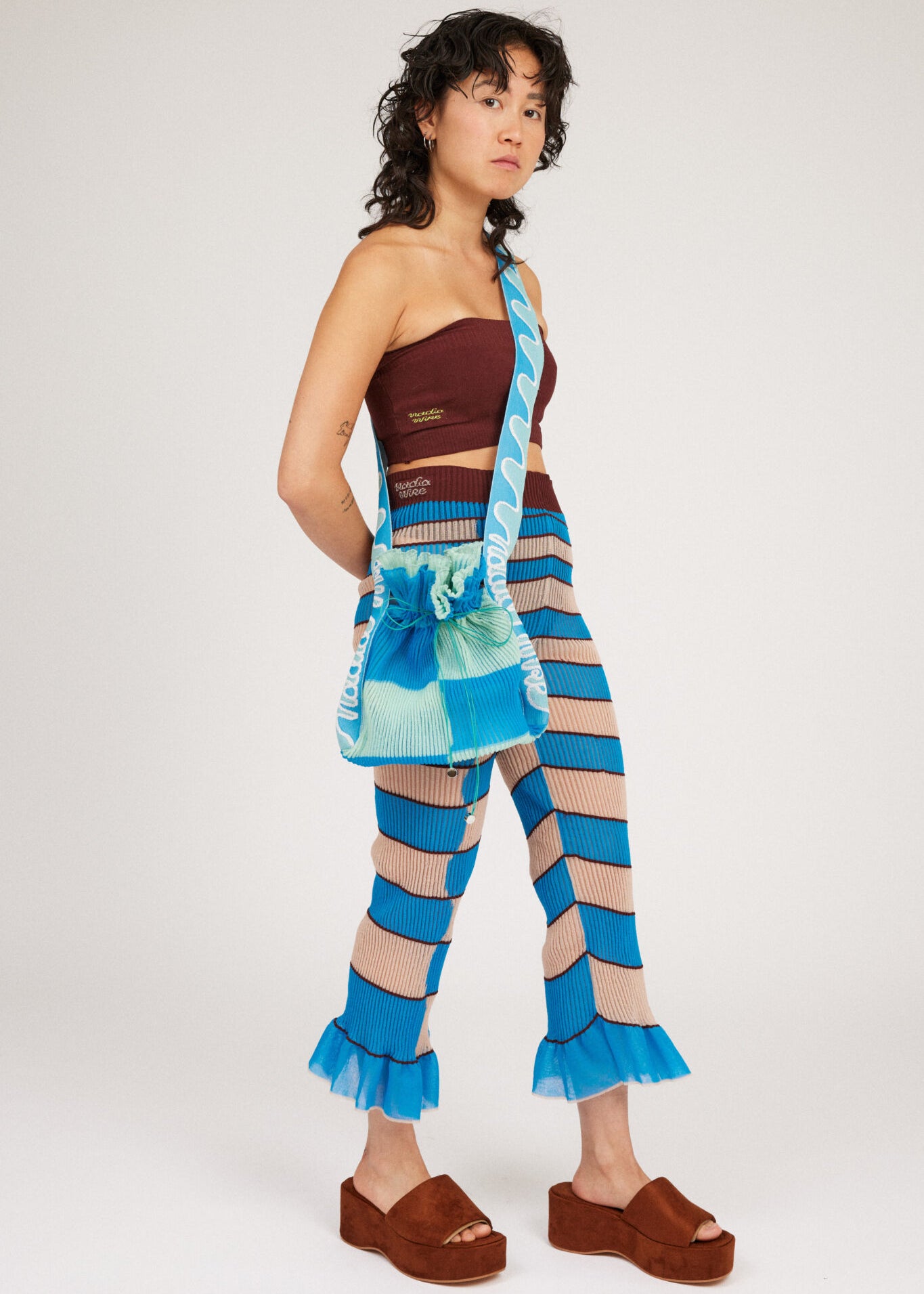 Twisted Frill Bag in blue and mint green is a knitted transparent crossbody cinch bag in twisted chess stripes. Detailed with ruffles, a logo jacquard strap and an adjustable opening.