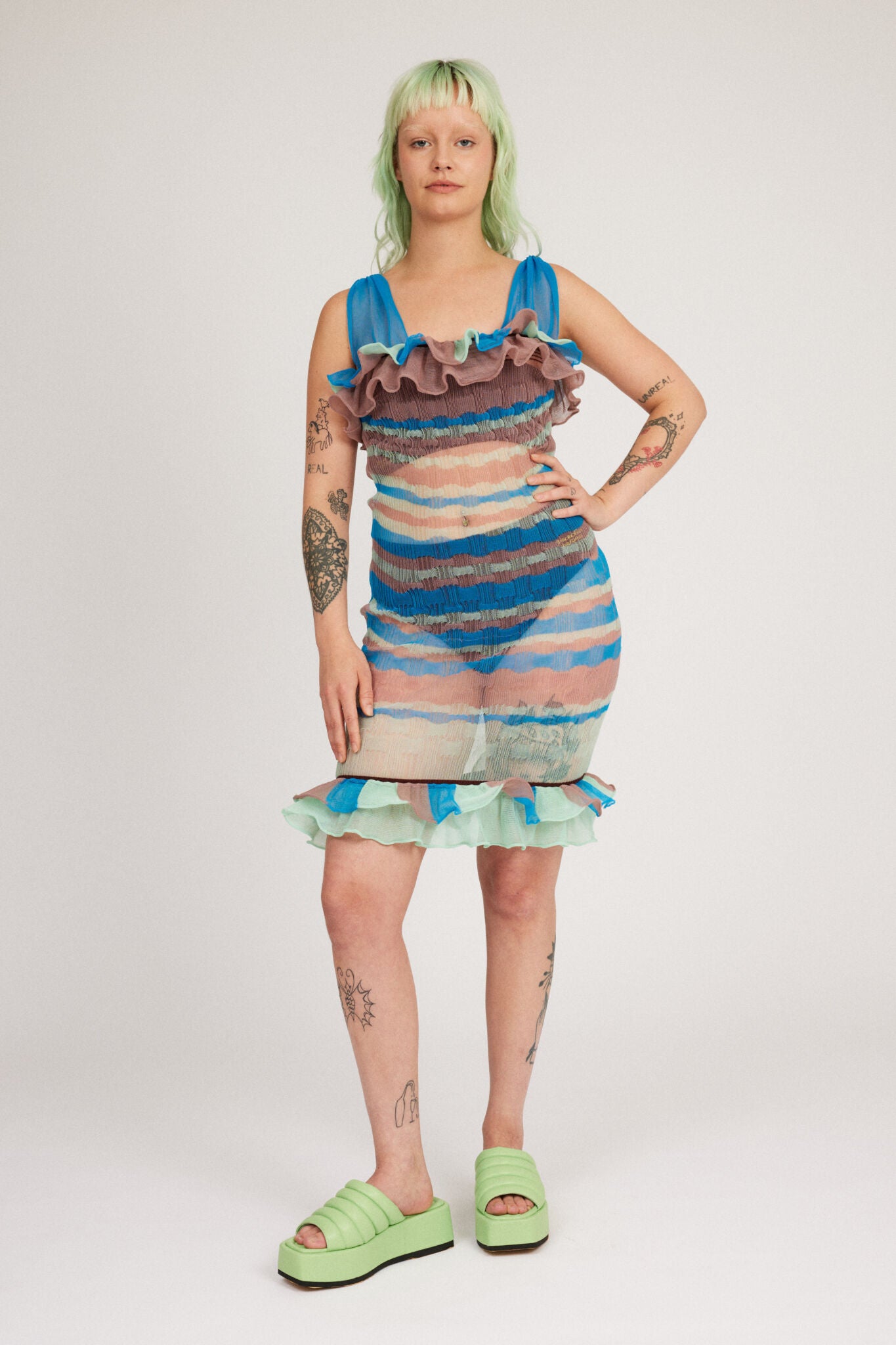 Loveable Dress in blue and mint is a transparent knitted strap dress in bold stripes with a ribbed bubble texture. The textile is lightweight, delicate and very flexible. The dress has a body fitted silhouette that adapts to the body. Detailed with frills.