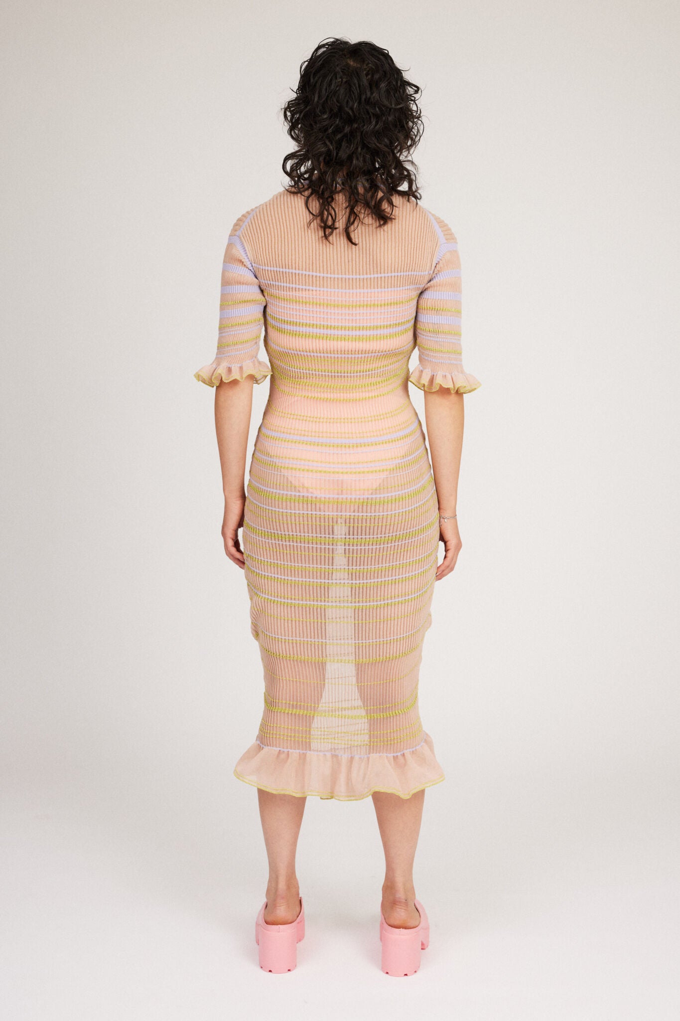 Sweet Secret Dress in peach blonde is a transparent knitted short sleeved high neck dress in gradient stripes with shimmery metallized yarn. The textile is lightweight, delicate and very flexible. The dress has a body fitted silhouette that adapts to the body. Detailed with frills and a logo in the back of neck.