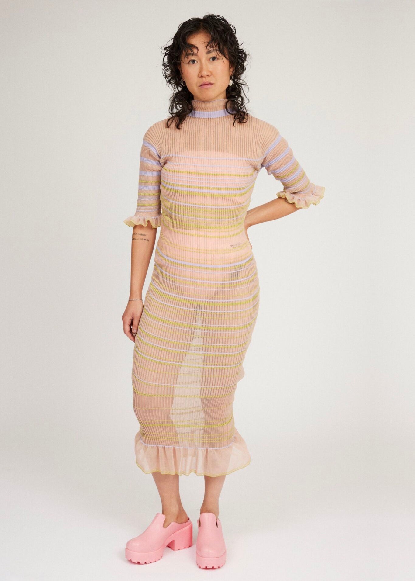 Sweet Secret Dress in peach blonde is a transparent knitted short sleeved high neck dress in gradient stripes with shimmery metallized yarn. The textile is lightweight, delicate and very flexible. The dress has a body fitted silhouette that adapts to the body. Detailed with frills and a logo in the back of neck.