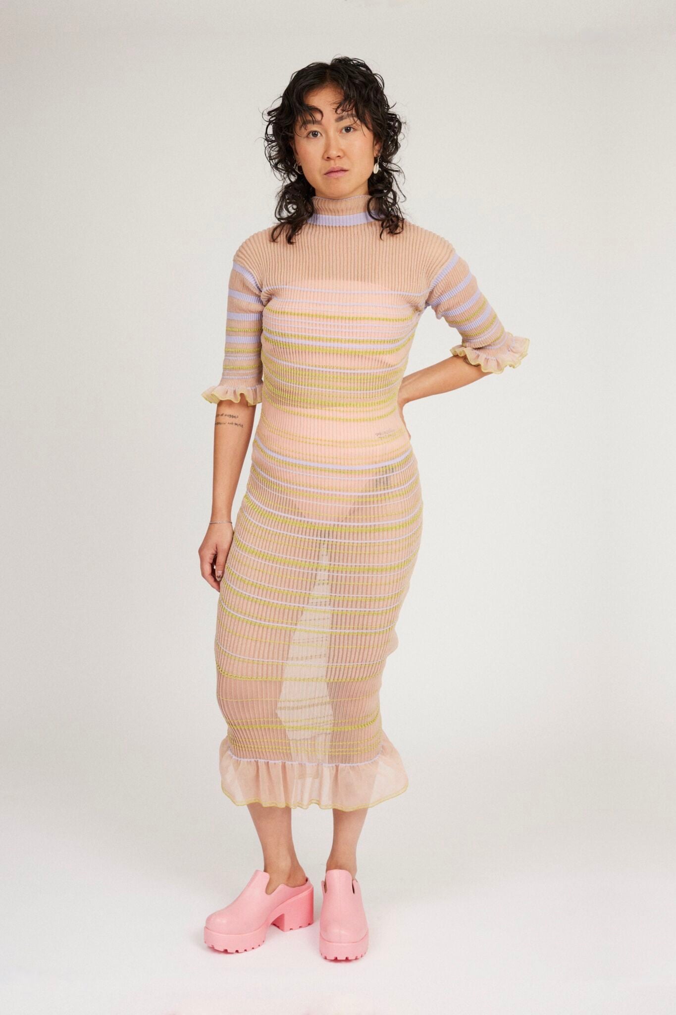 Sweet Secret Dress in peach blonde is a transparent knitted short sleeved high neck dress in gradient stripes with shimmery metallized yarn. The textile is lightweight, delicate and very flexible. The dress has a body fitted silhouette that adapts to the body. Detailed with frills and a logo in the back of neck.
