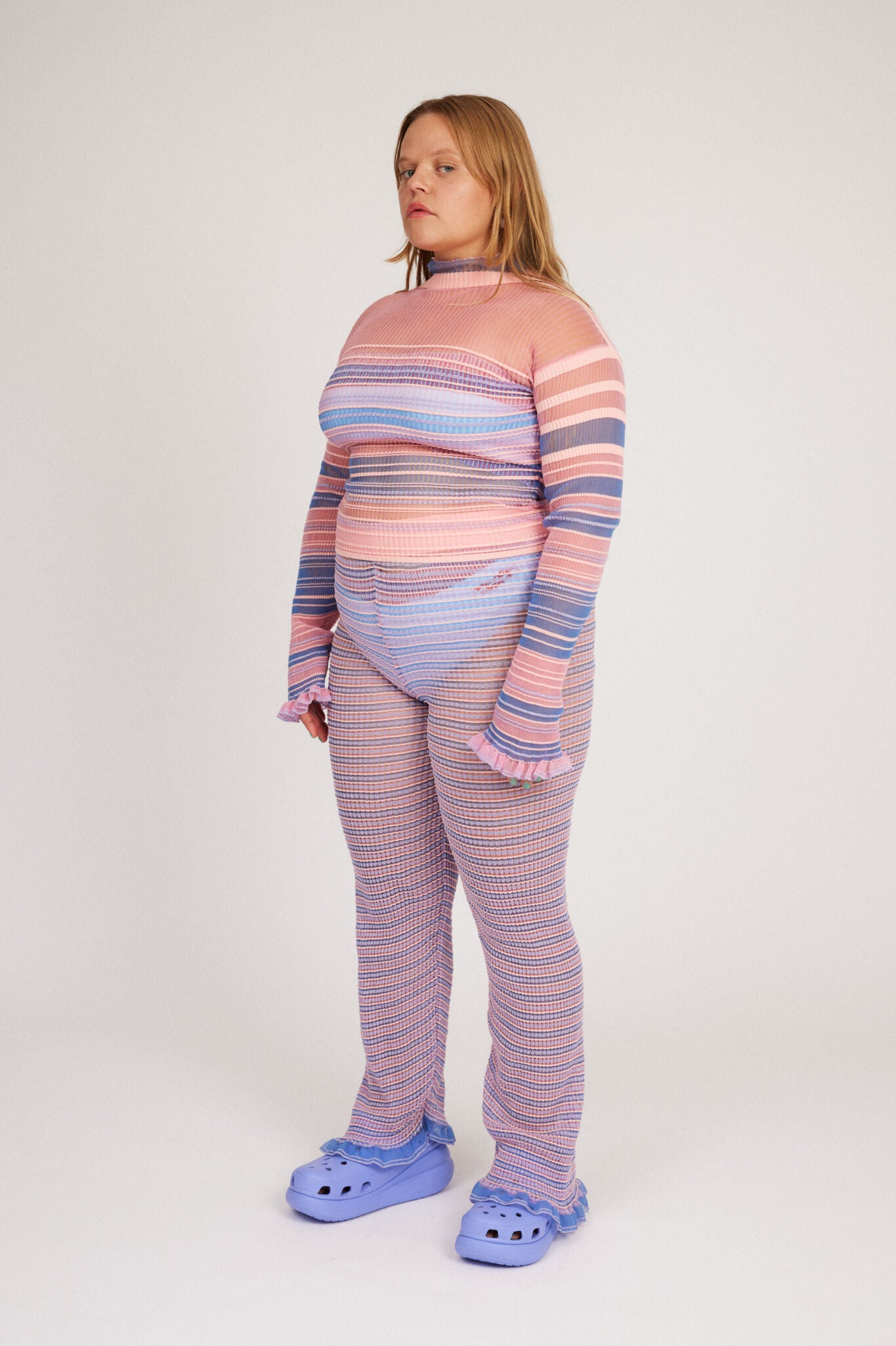 Sweet Secret Jumper in pink and powder blue is a knitted transparent high neck jumper in all over bold stripes detailed with shimmery metallized yarn. The textile is lightweight, delicate and very flexible. The jumper has a body fitted silhouette that adapts to the body. Detailed with frills and a logo in the back of the neck.