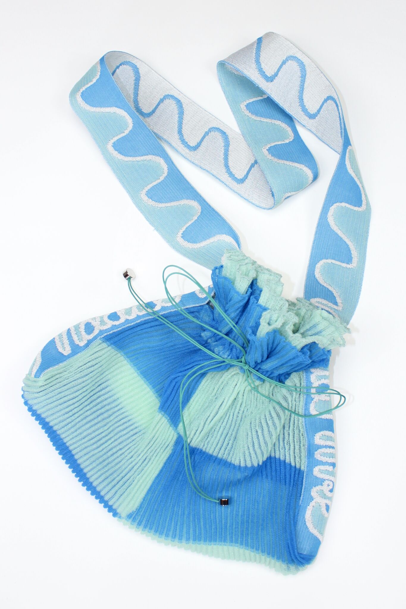 Twisted Frill Bag in blue and mint green is a knitted transparent crossbody cinch bag in twisted chess stripes. Detailed with ruffles, a logo jacquard strap and an adjustable opening.