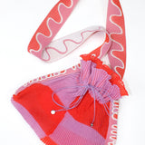 Twisted Frill Bag in coral red and lavender is a knitted transparent crossbody cinch bag in twisted chess stripes. Detailed with ruffles, a logo jacquard strap and an adjustable opening. The textile is lightweight, delicate and flexible and has ribbed texture.