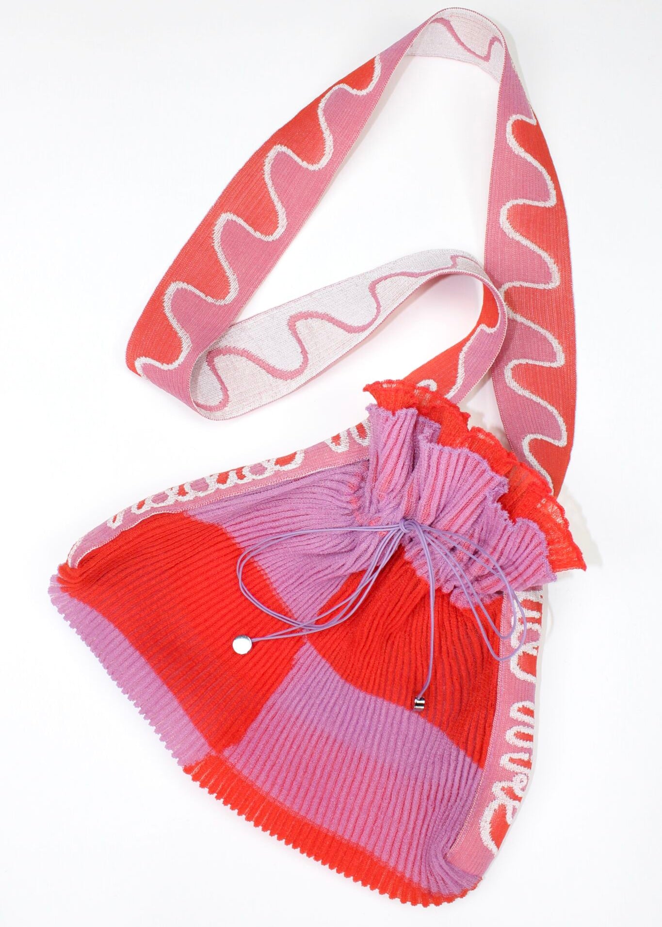 Twisted Frill Bag in coral red and lavender is a knitted transparent crossbody cinch bag in twisted chess stripes. Detailed with ruffles, a logo jacquard strap and an adjustable opening. The textile is lightweight, delicate and flexible and has ribbed texture.