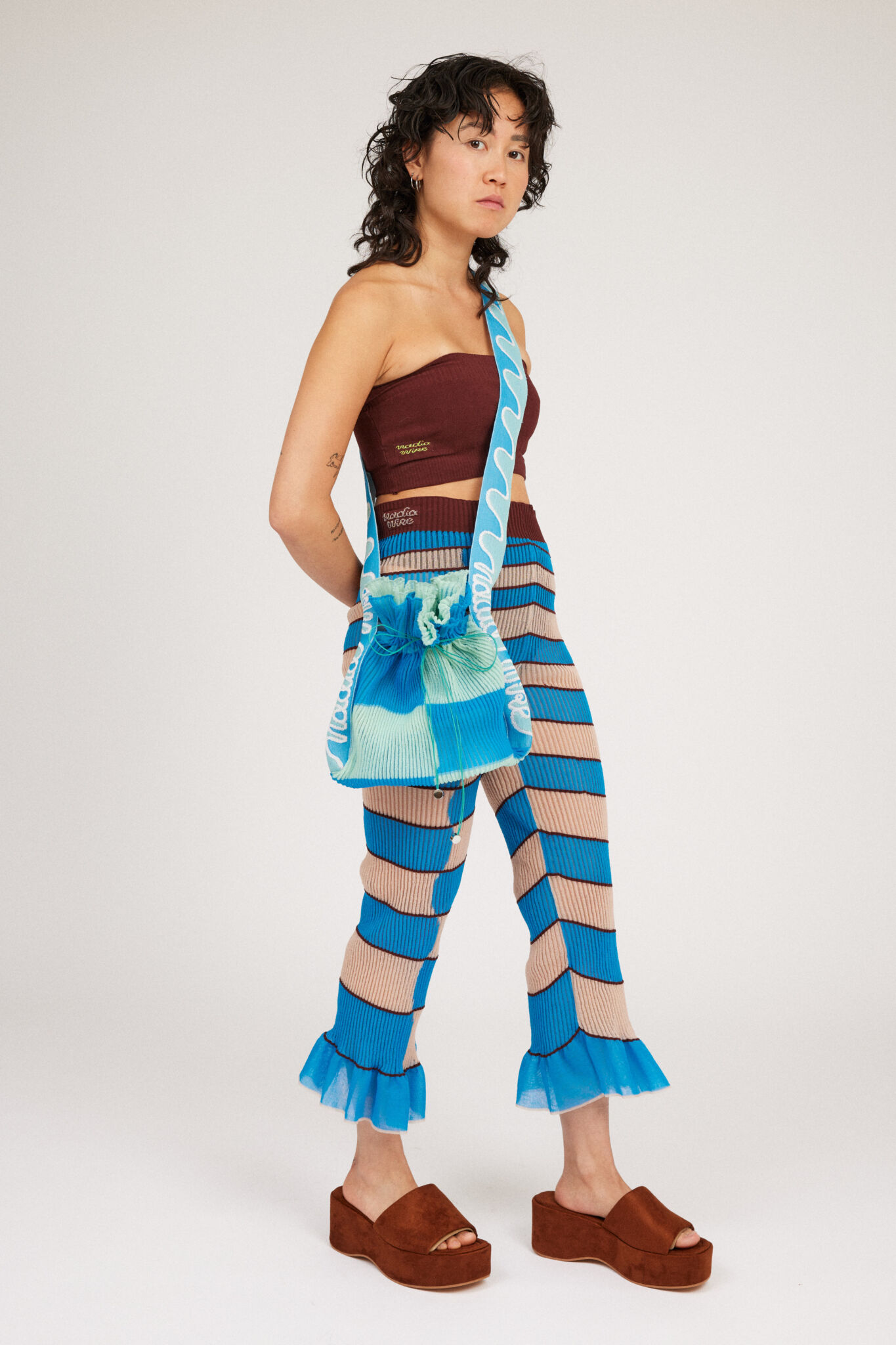 Twisted Frill Bag in blue and mint green is a knitted transparent crossbody cinch bag in twisted chess stripes. Detailed with ruffles, a logo jacquard strap and an adjustable opening.