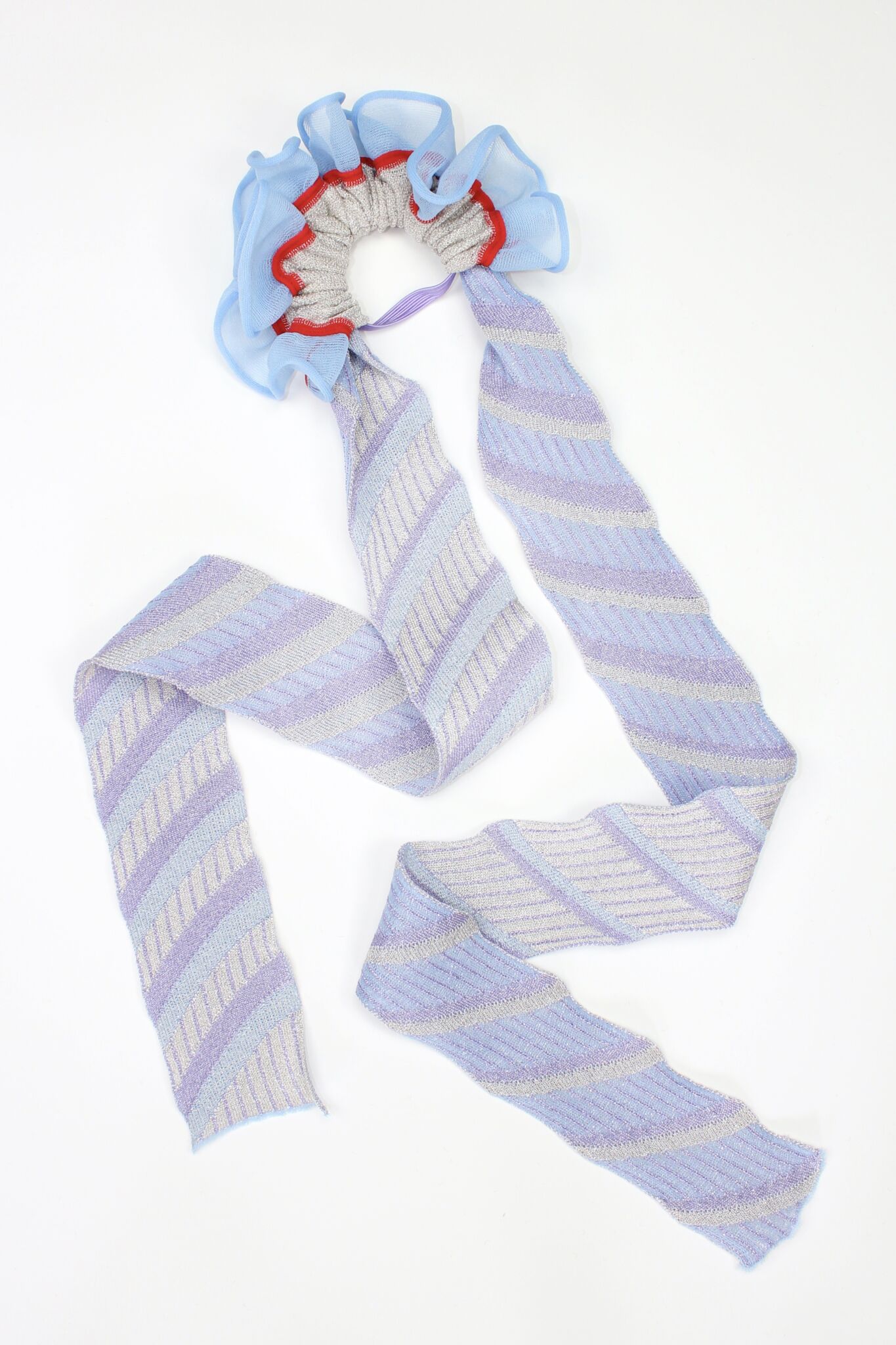 Gazania Scrunchie in light blue and silver is a knitted scrunchie with striped jacquard ties. Made of transparent and shimmery yarns.