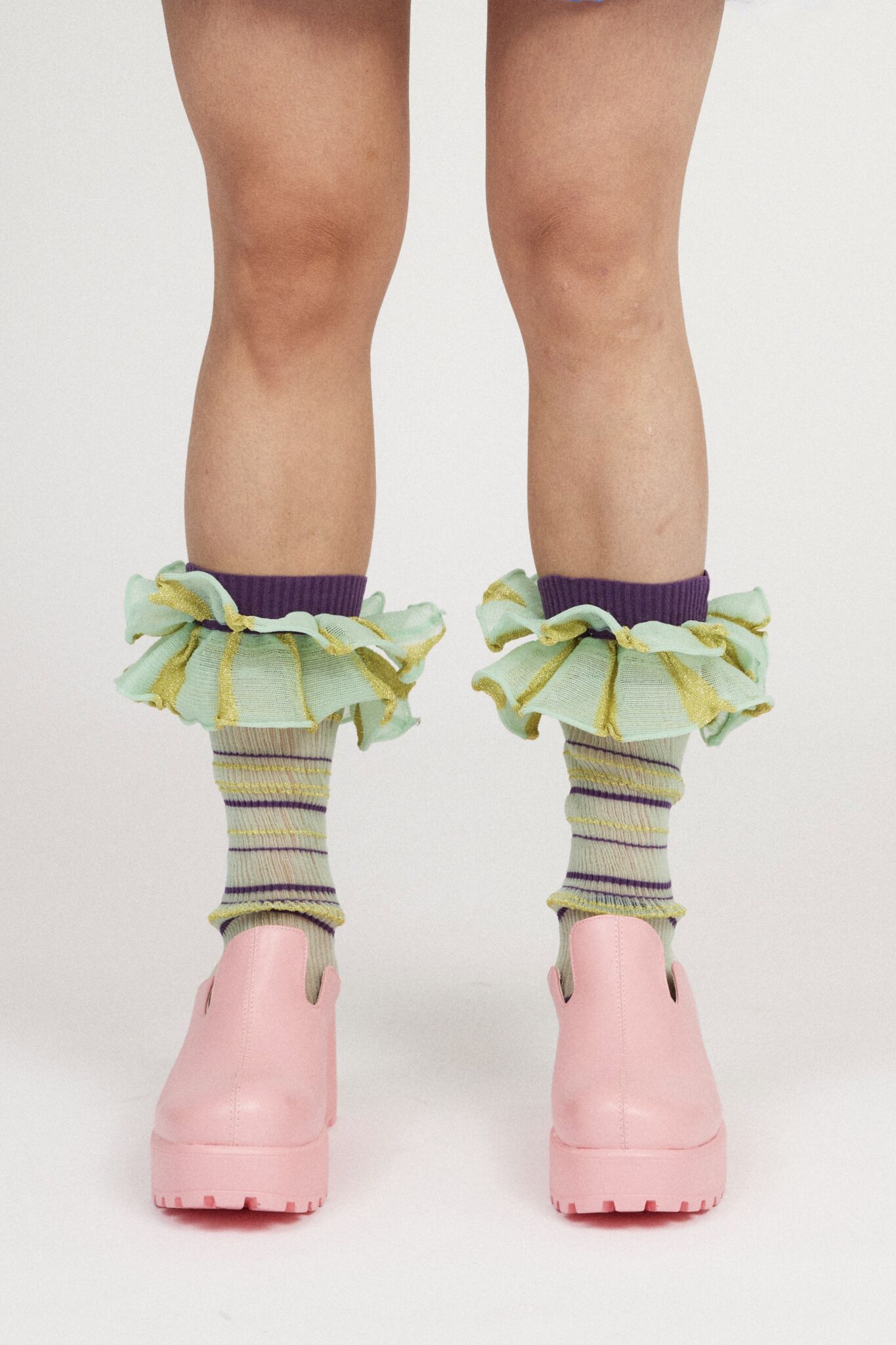 Mini Confetti Frills in mint green and purple are a knitted pair of transparent striped ruffle frills with a ribbed texture. The textile is lightweight, delicate and very flexible. Can be worn on both the arms and legs.