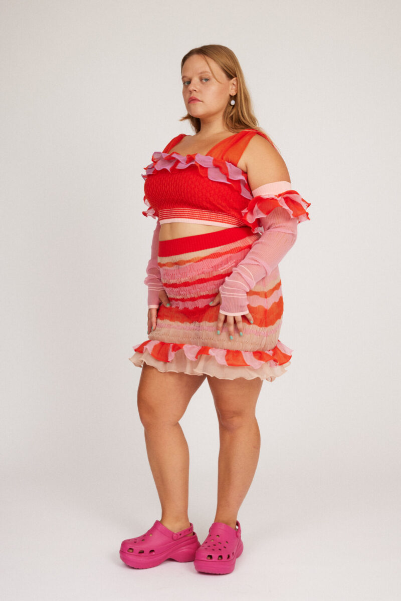 Loveable Skirt in coral red and peach blonde is a transparent knitted mini skirt with a ribbed bubble texture. The textile is lightweight, delicate and very flexible. The skirt has a body fitted silhouette that adapts to the body. Detailed with frills and a logo in the back.