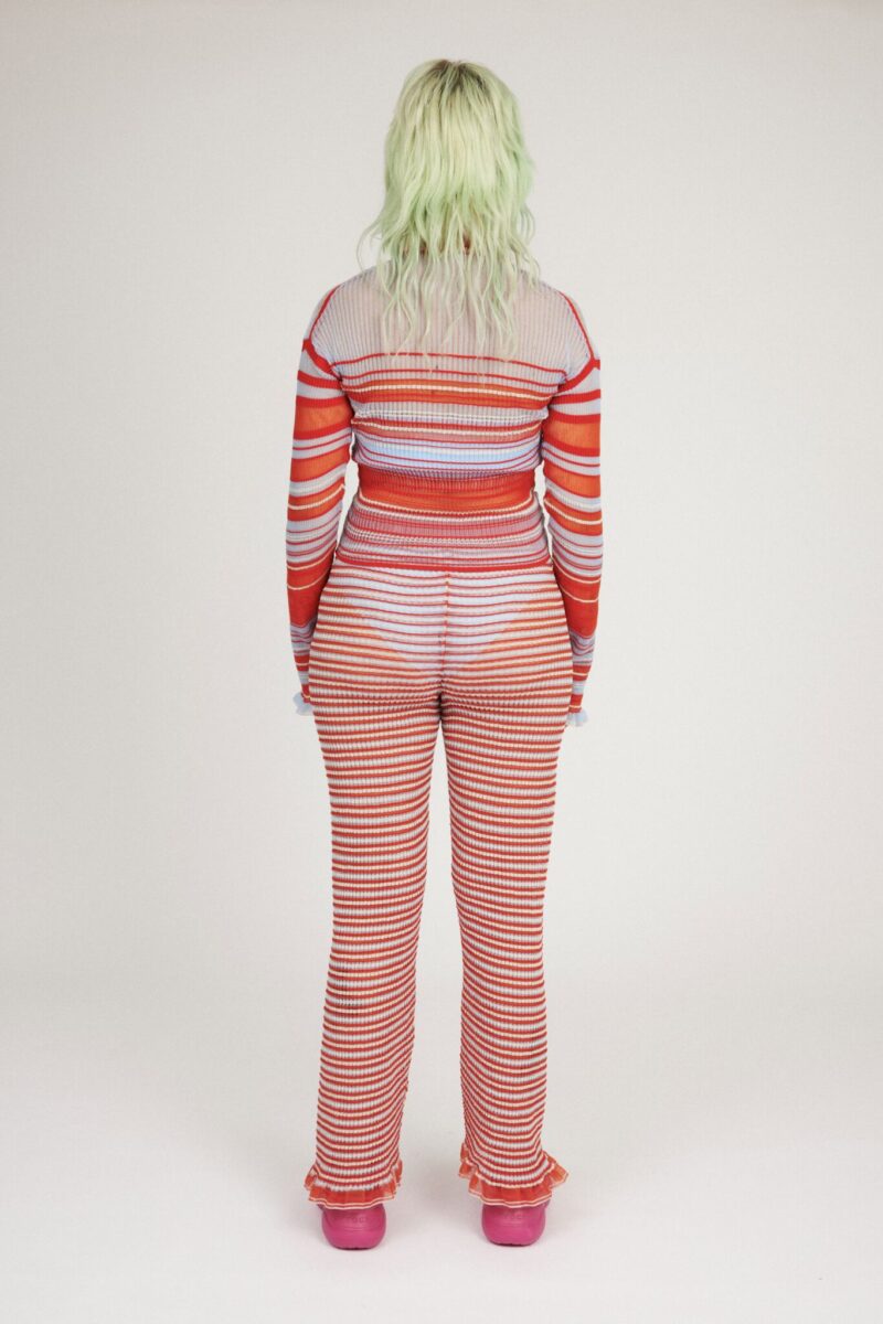 Sweet Secret Jumper in coral red and light blue is a knitted transparent high neck jumper in all over bold stripes detailed with shimmery metallized yarn. The textile is lightweight, delicate and very flexible. The jumper has a body fitted silhouette that adapts to the body. Detailed with frills and a logo in the back of the neck.