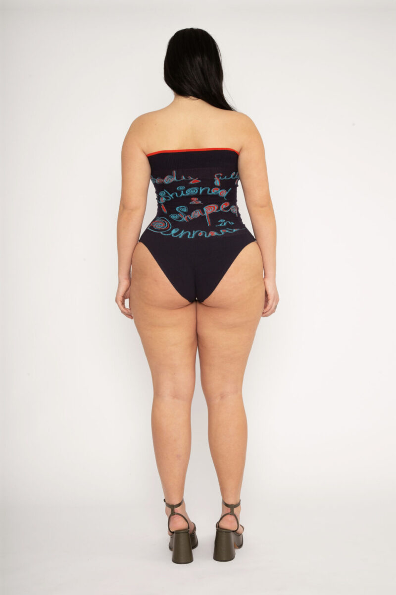 Fashioned Bodysuit in navy and turquoise is a jacquard knitted strapless body with 3D statement artwork in bold colours. Knitted in a fitted, yet very flexible material that adapts to the body and has a slight shaping effect. Detailed with a ribbed upper rim to keep it in place. The Fashioned Bodysuit is a tribute to our core values and production methods, with the text in the front stating ”Shaped & fashioned Wire body” and the back ”Body fully fashioned & shaped in Denmark”. Fully fashioning is a waste minimizing technique used when knitting all our garments. Available in 3 different colours and sizes.