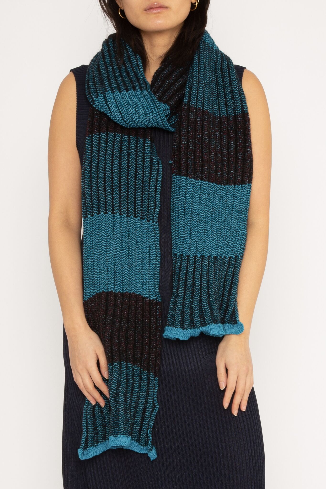 Checked Scarf in turquoise and black is a knitted merino wool and mohair scarf in checked stripes. The textile is soft, airy and lightweight – and most important non-itchy. Detailed with red yarn in the black areas.